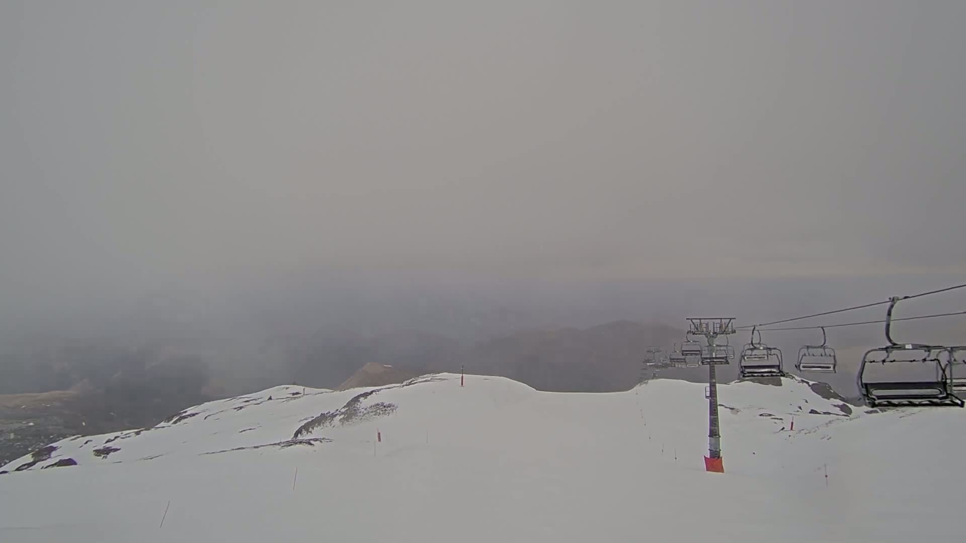 A chairlift ascends a snow-covered mountain in foggy conditions.