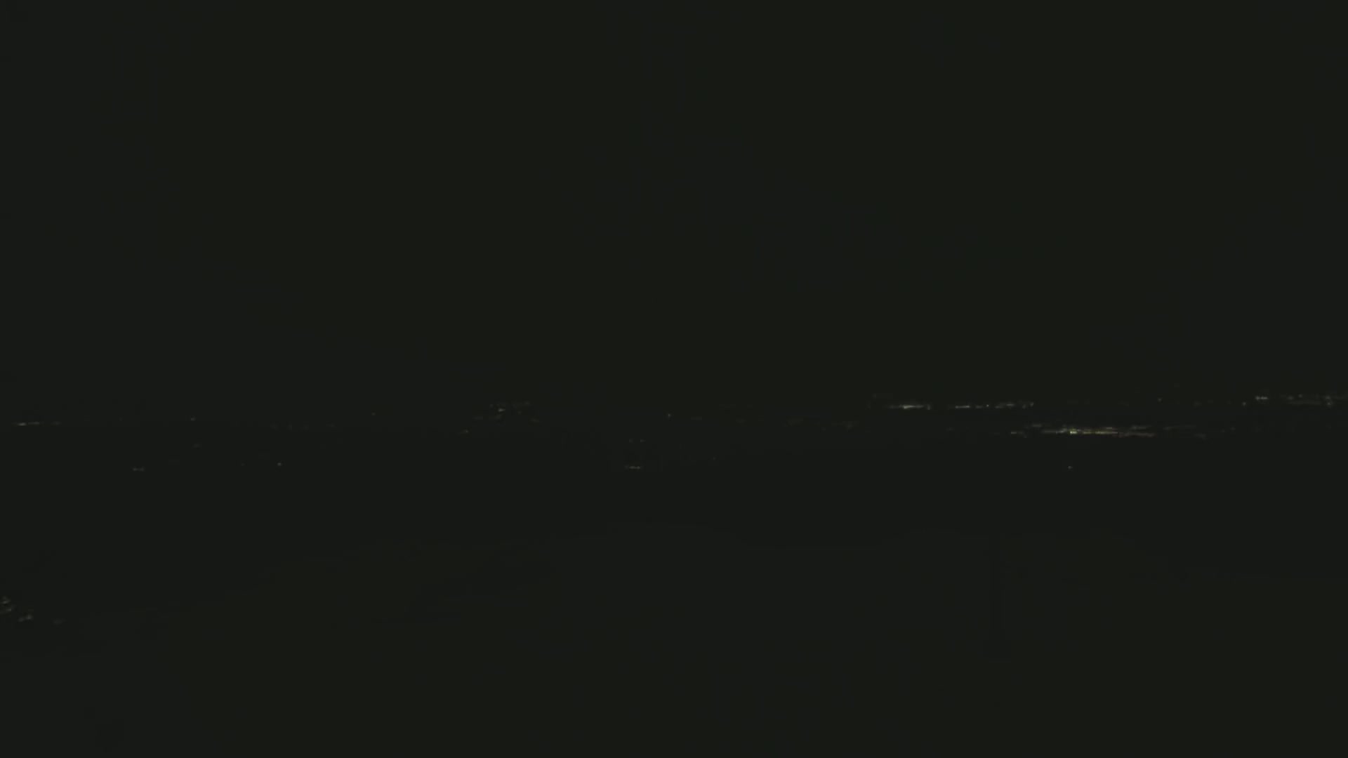 A dark, nighttime view shows a distant line of faint lights from a city or town.
