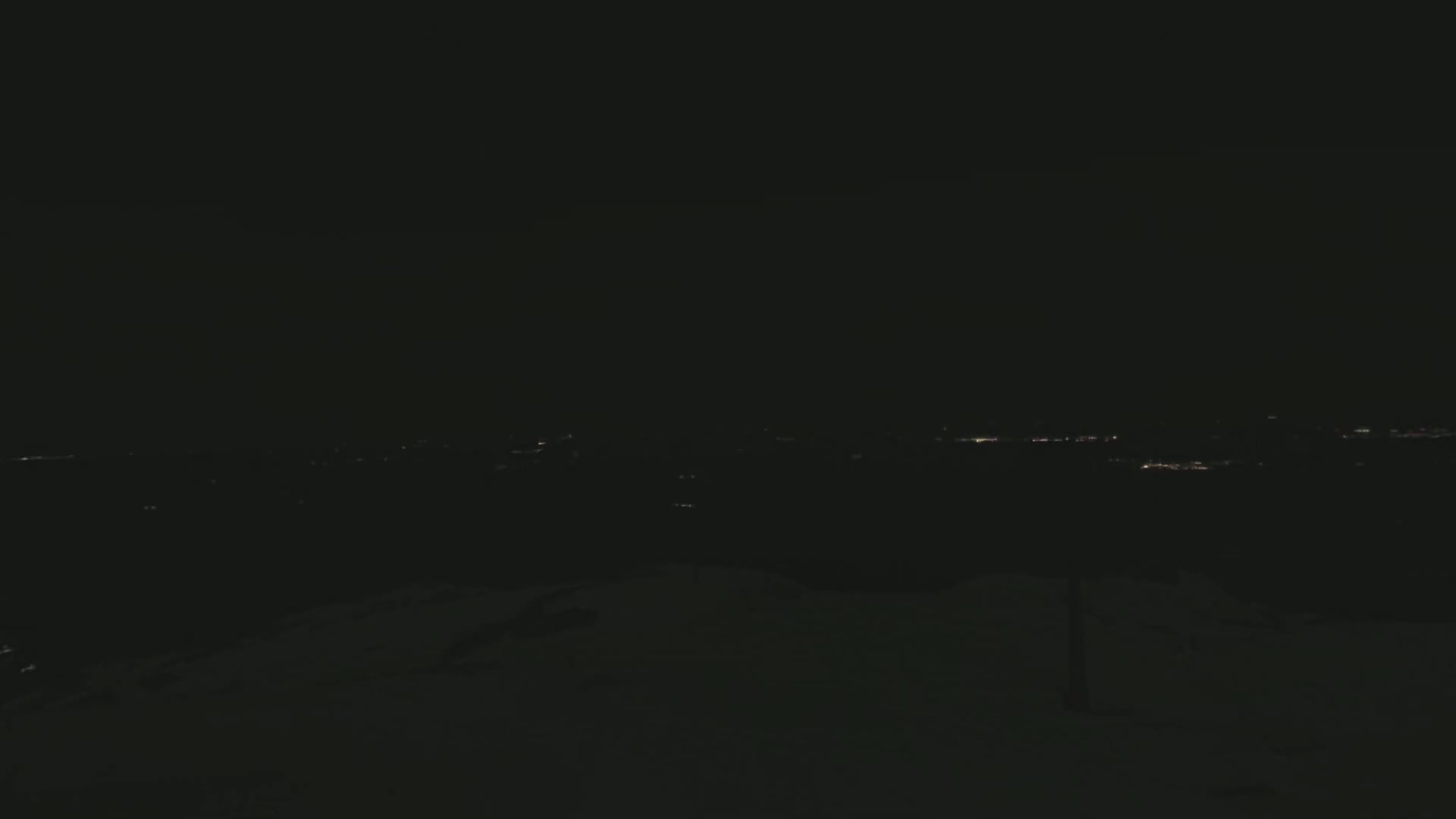 A snowy, nighttime landscape shows a distant line of faint city lights.