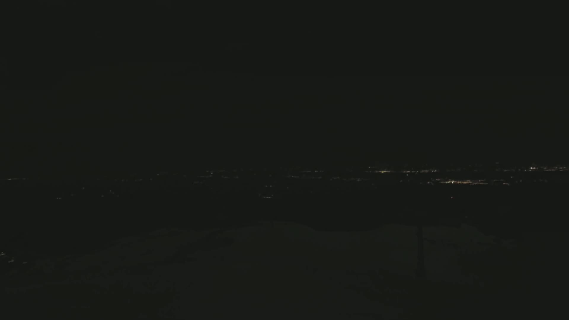 A dark, nighttime view shows a distant city's lights spread across a low horizon.