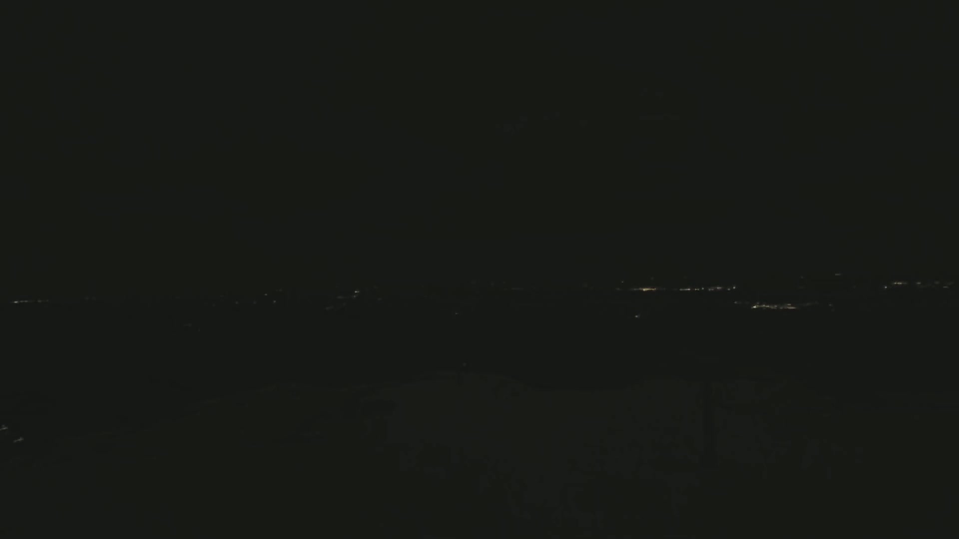 A distant line of faint lights is visible across a dark, nighttime landscape.