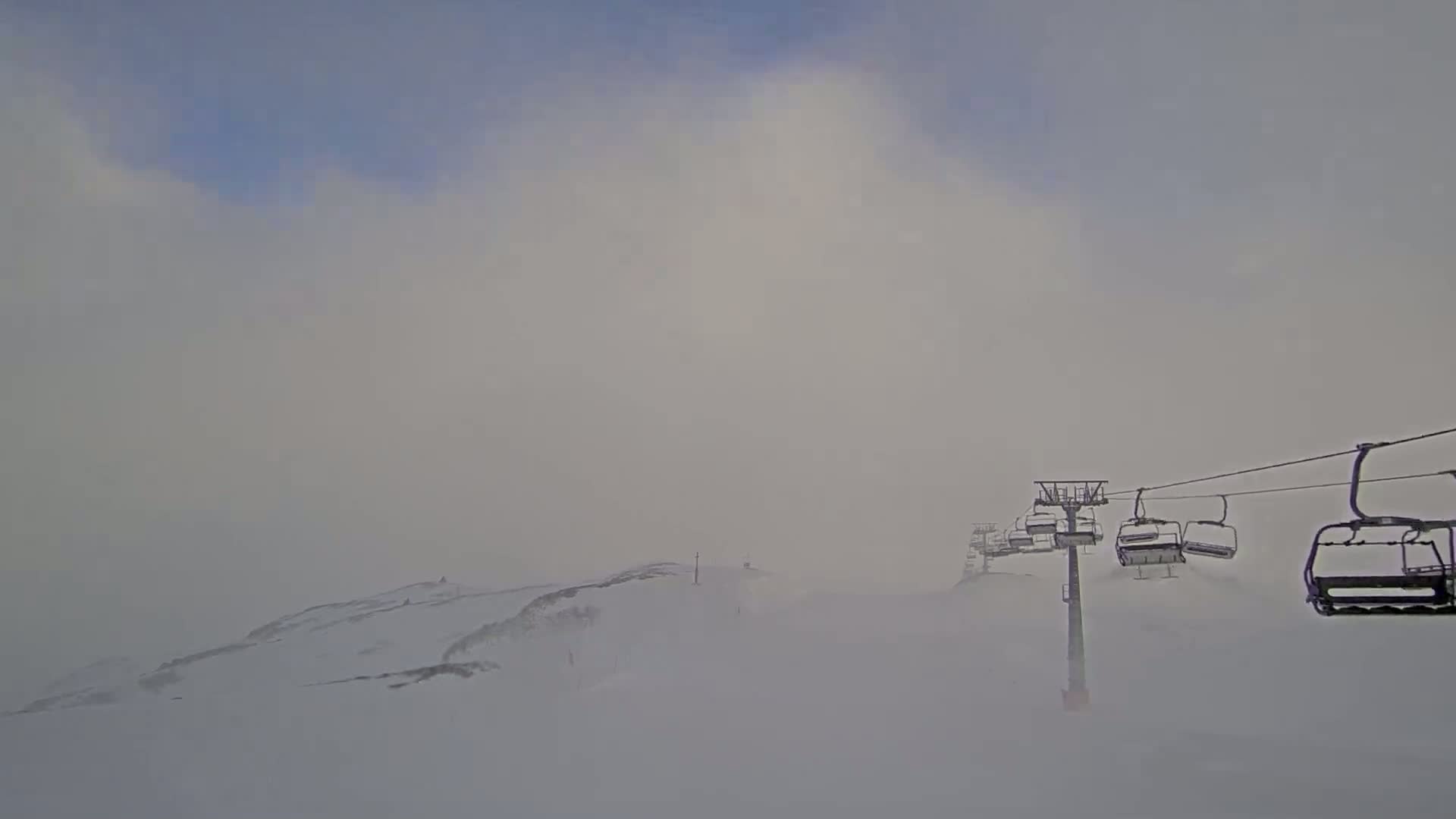 A chairlift ascends a snow-covered mountain in foggy conditions.