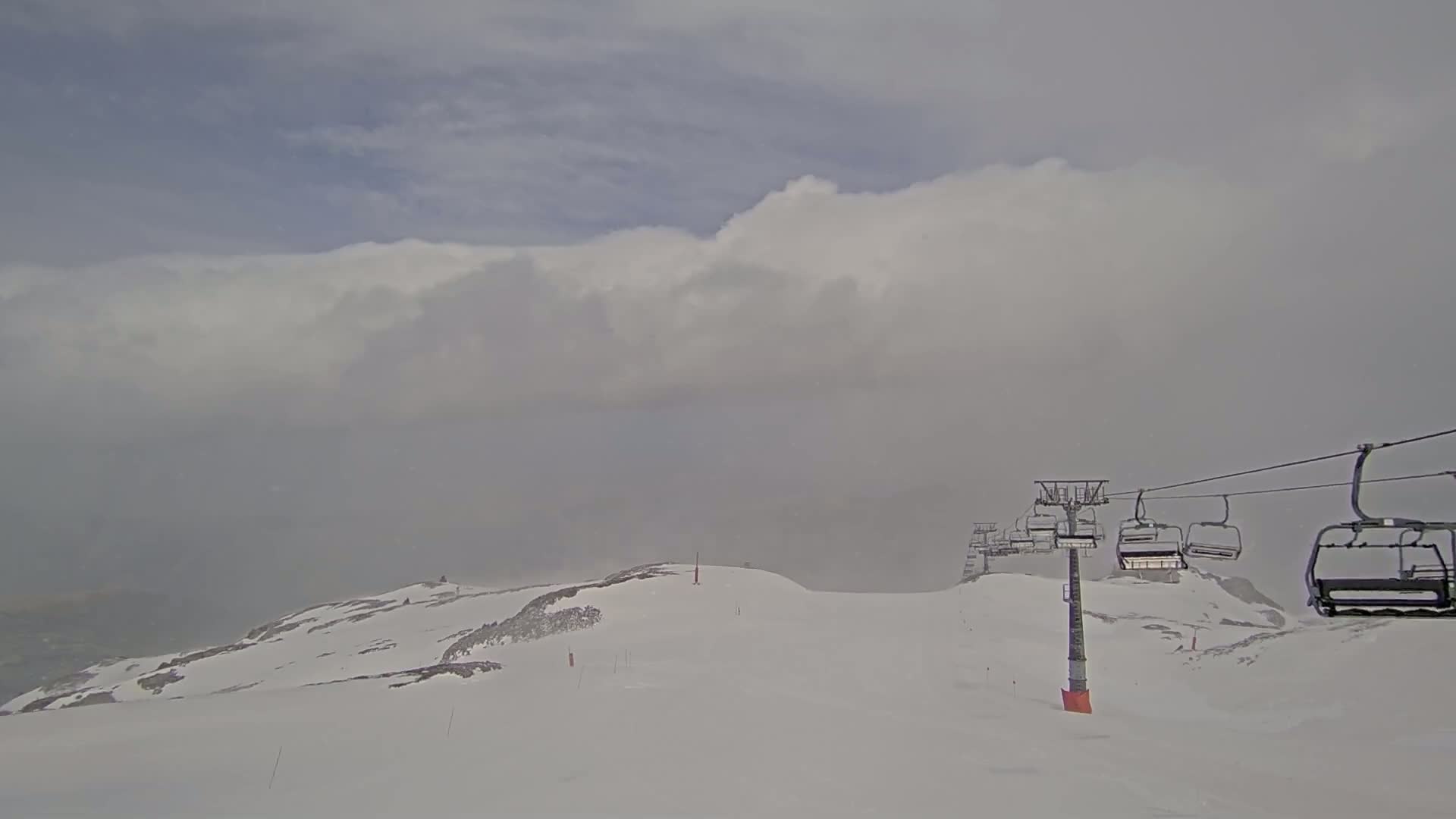 A snow-covered mountain slope with a chairlift and low-hanging clouds under overcast skies.