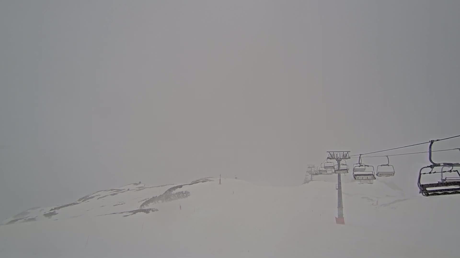 A chairlift ascends a snow-covered mountain in foggy conditions.