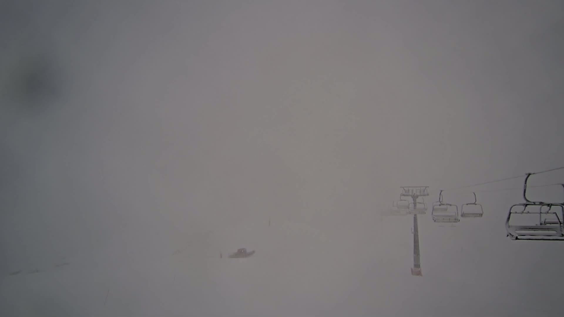 A snow-covered ski lift with empty chairs is barely visible in a heavy snowstorm.