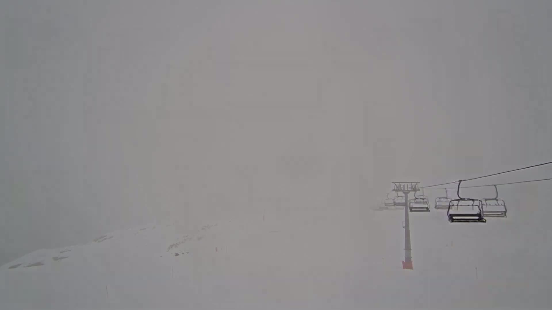 A ski lift with several empty chairlifts is visible through heavy fog or snow on a snowy landscape.
