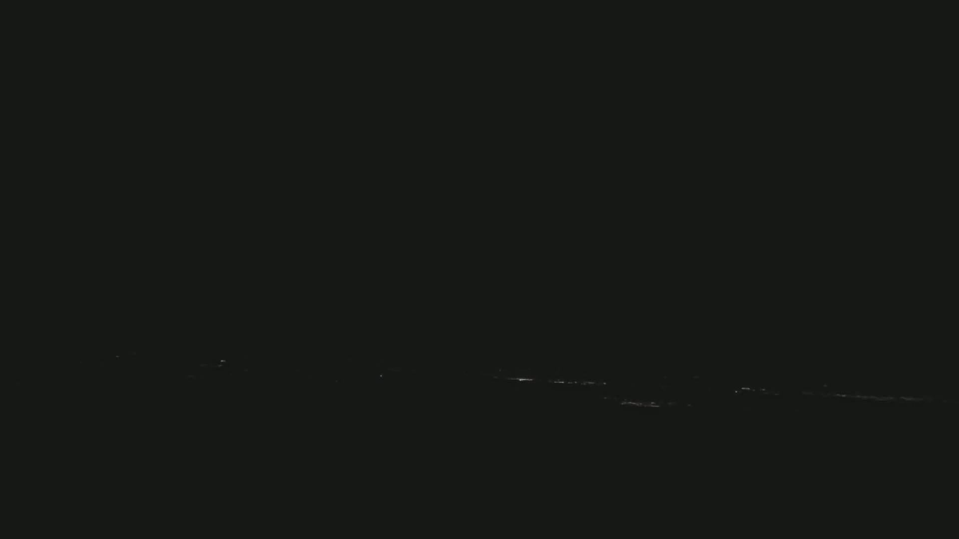 A distant line of faint lights is visible on a dark, nighttime horizon.
