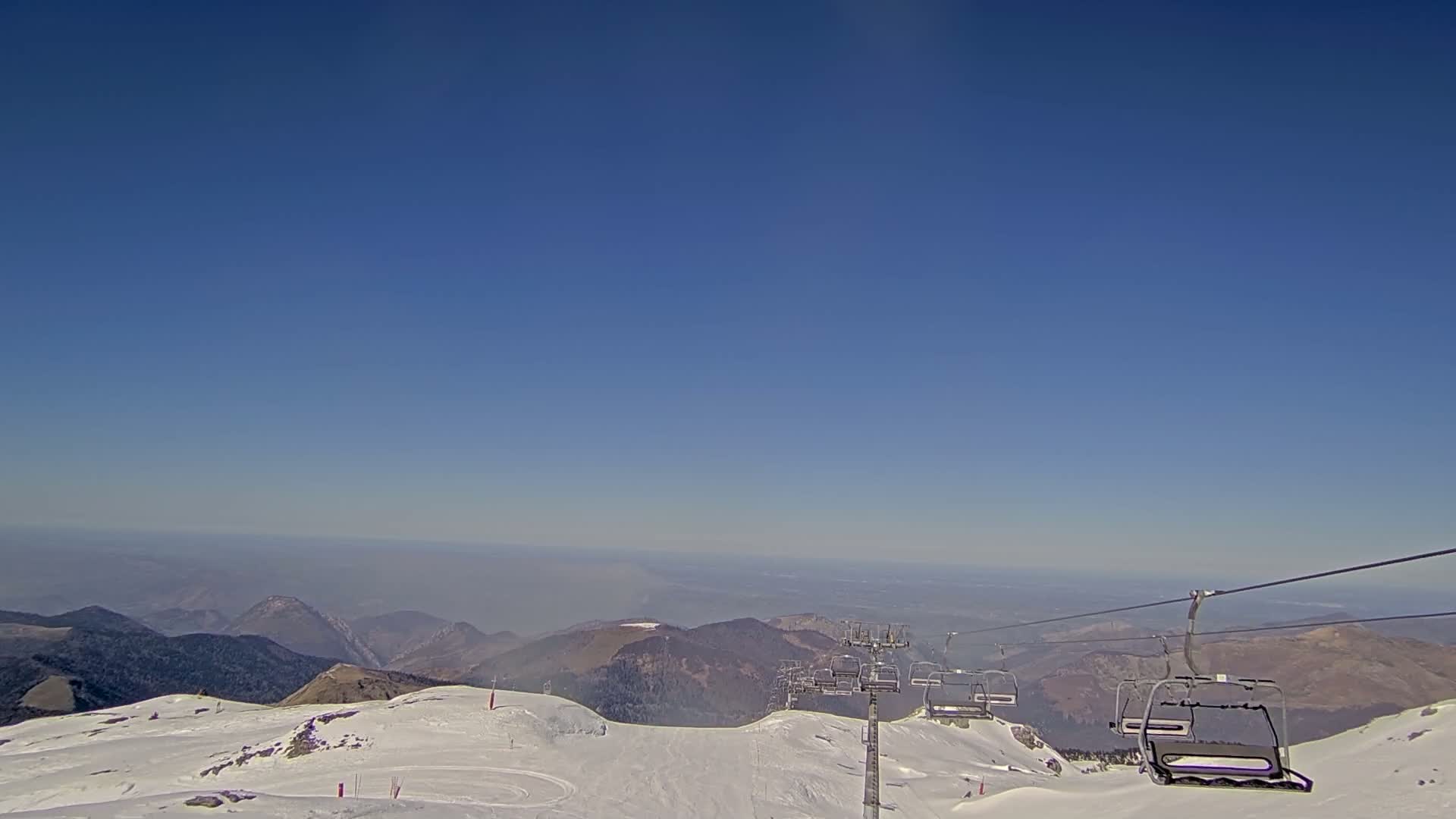A chairlift ascends a snow-covered mountain range under a clear blue sky.