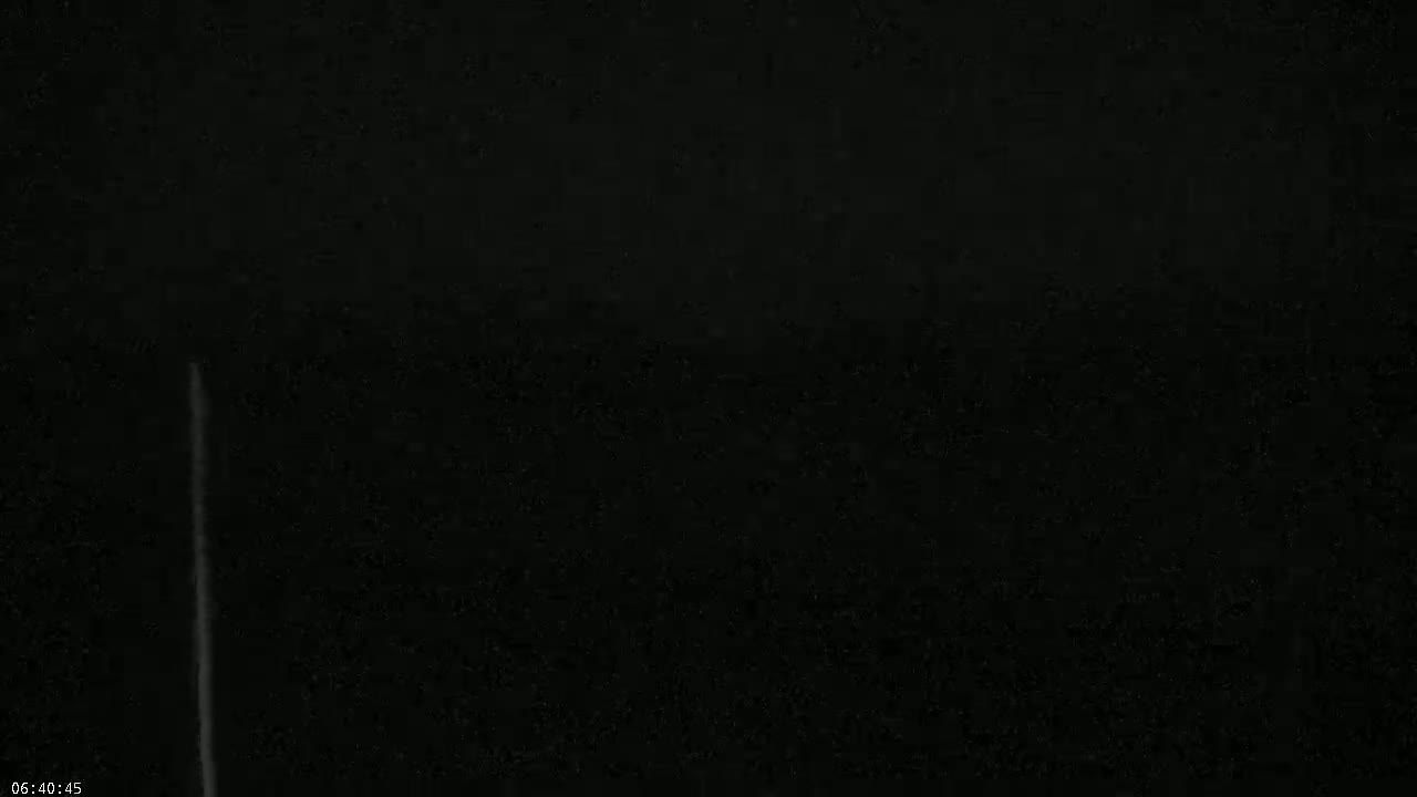 A thin, vertical white streak appears against a completely dark, nighttime sky.