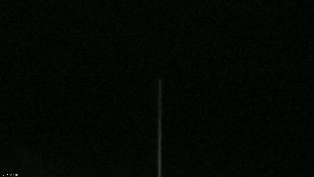 A thin, vertical, bright streak is visible against a dark, nighttime sky.