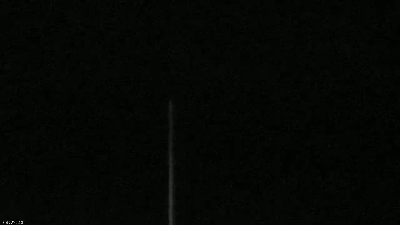 A thin, vertical streak of light is visible against a completely dark, nighttime sky.