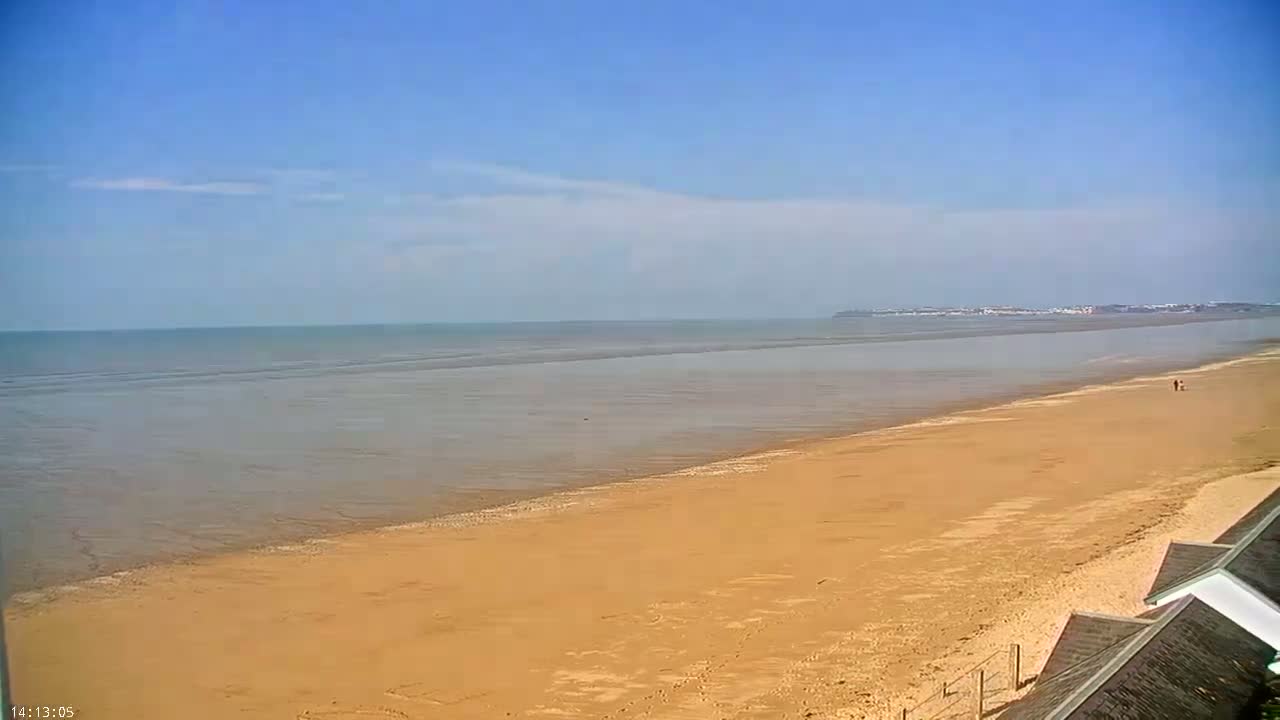 A long, sandy beach stretches to a calm sea under a mostly clear, bright blue sky.