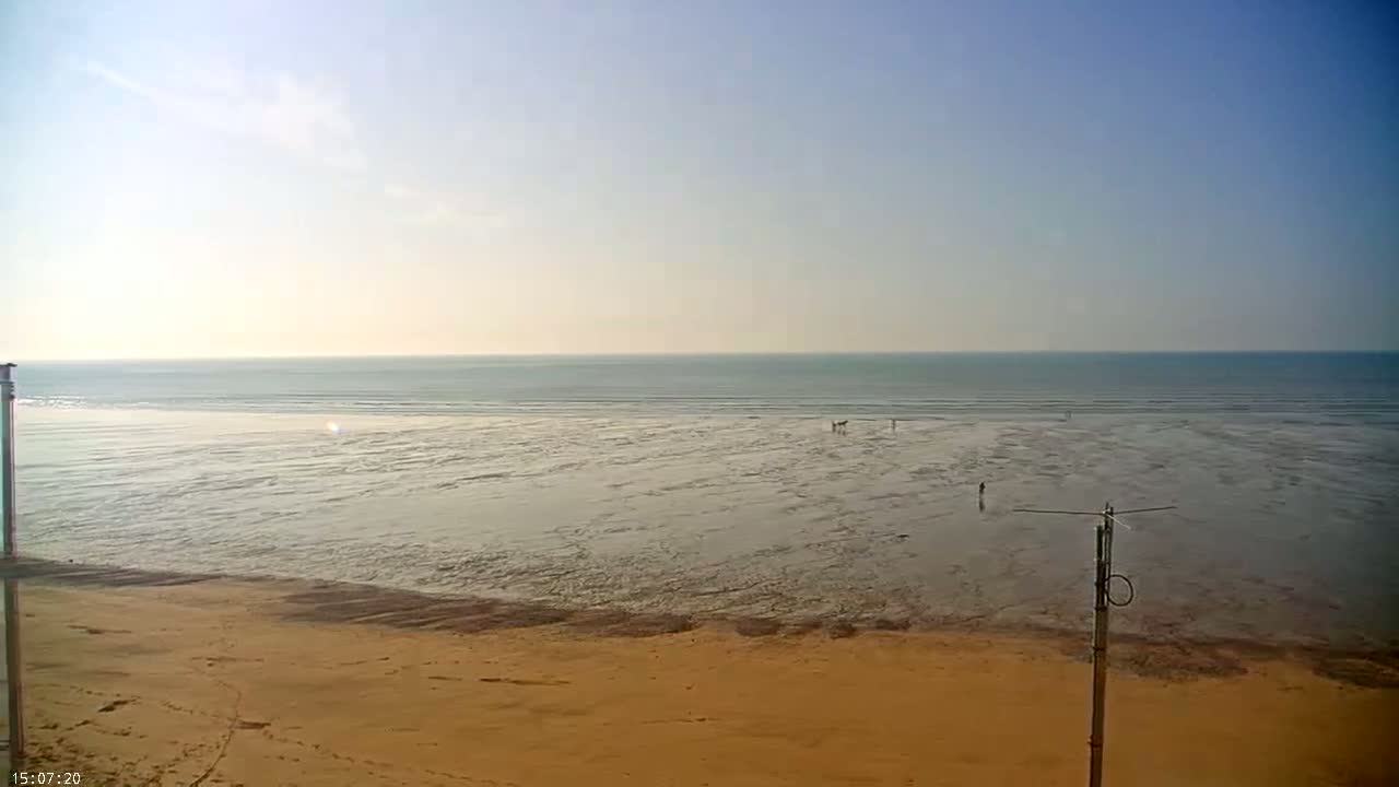 A wide sandy beach stretches out to a calm ocean under a clear, bright sky.