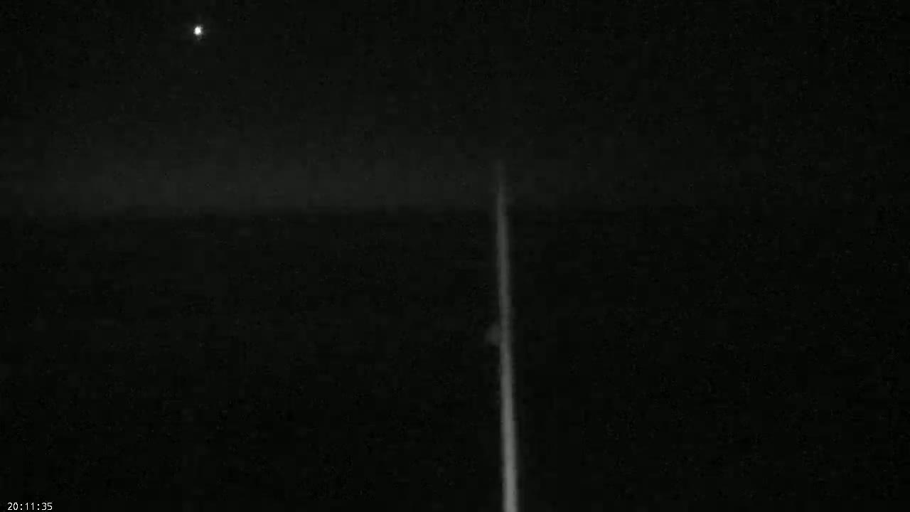 A bright light streaks across a dark, nighttime sky, with a single, dim star visible.