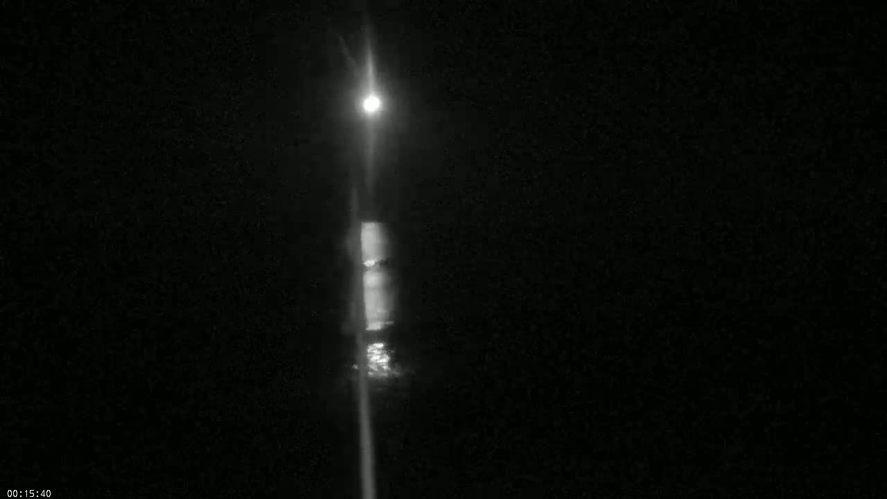A bright light shines down a dark, nighttime street, reflecting off a surface of water.