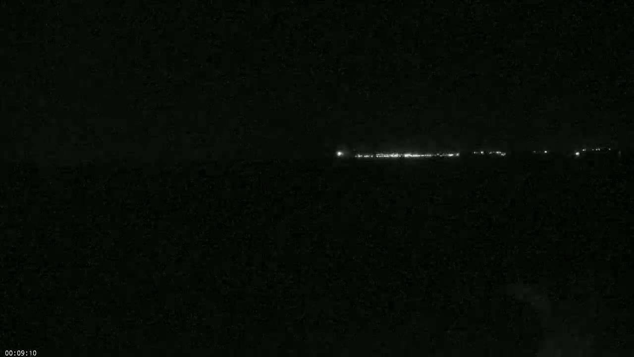 A long, faint line of lights is visible in the distance on a dark, nighttime horizon.