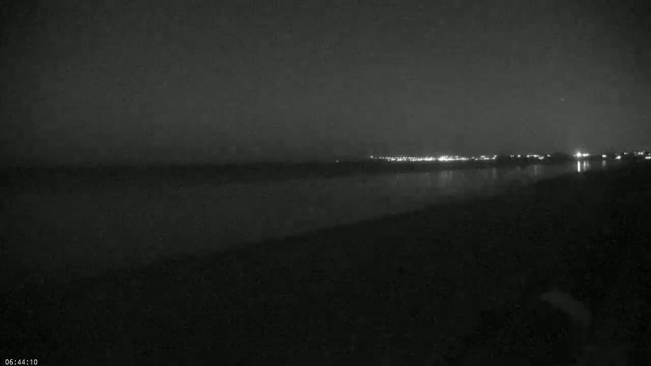 A dark, nighttime view of a body of water reflecting the distant lights of a city.