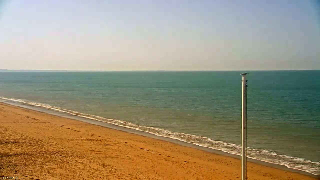 A sandy beach meets a calm, teal ocean under a clear, bright sky.