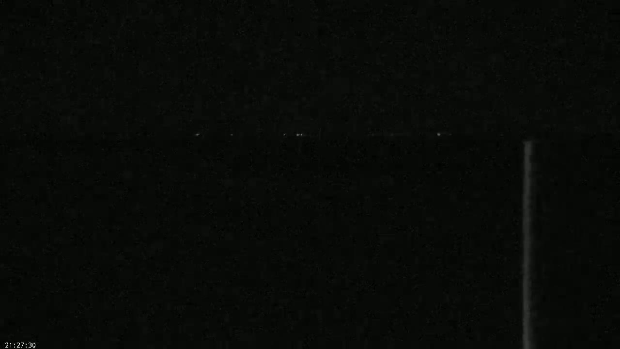 A dark, nighttime scene shows a few faint lights in the distance, possibly from a city or town, along a mostly dark horizon.