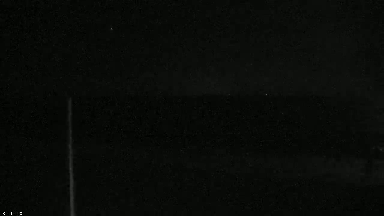 A thin, vertical streak of light is visible against a dark, nighttime sky speckled with faint stars.