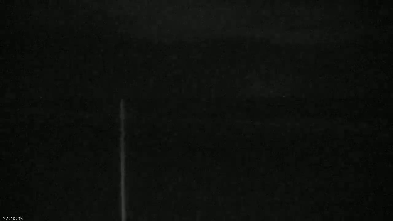 A thin, vertical, bright streak appears against a mostly dark, nighttime sky.