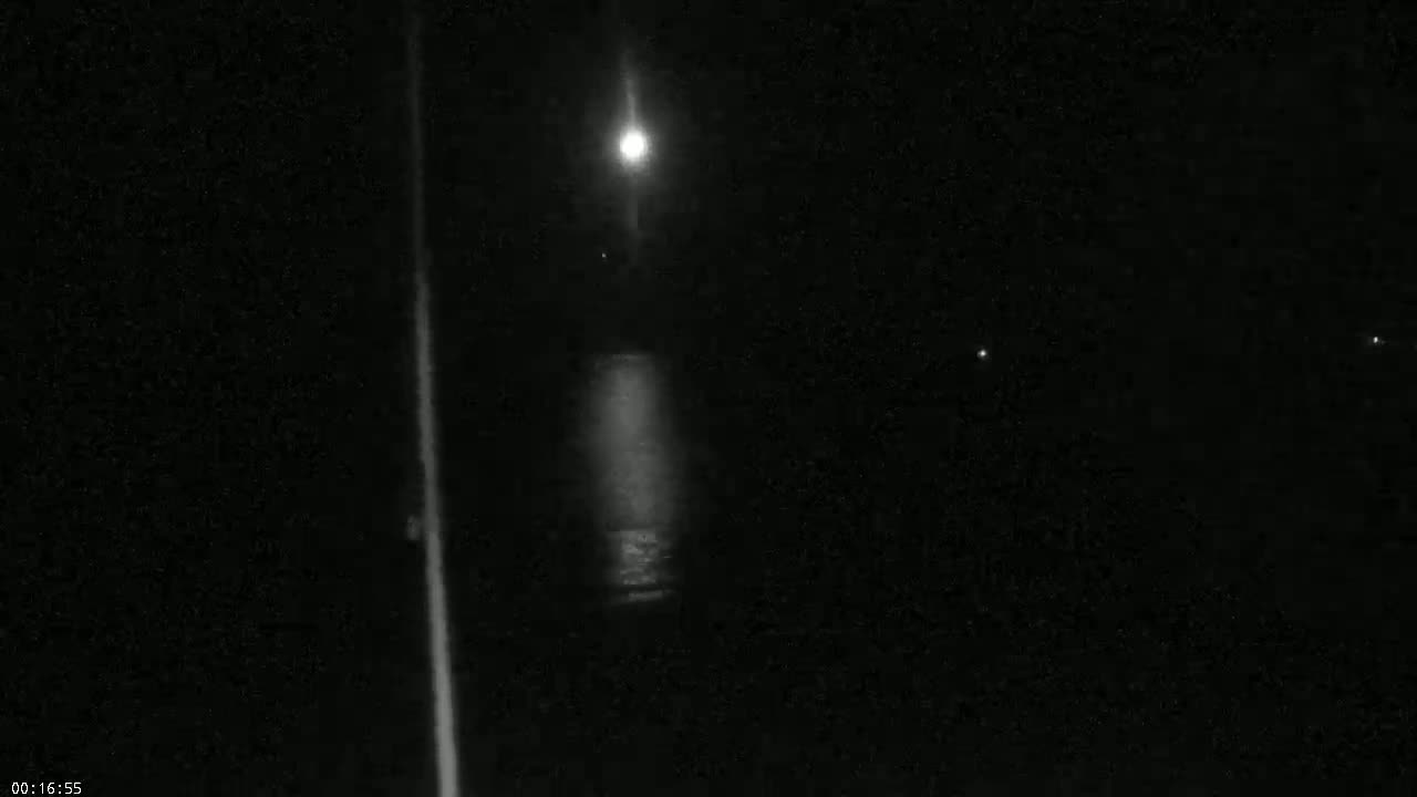 A bright light illuminates a dark, nighttime scene, with faint additional lights visible in the distance.