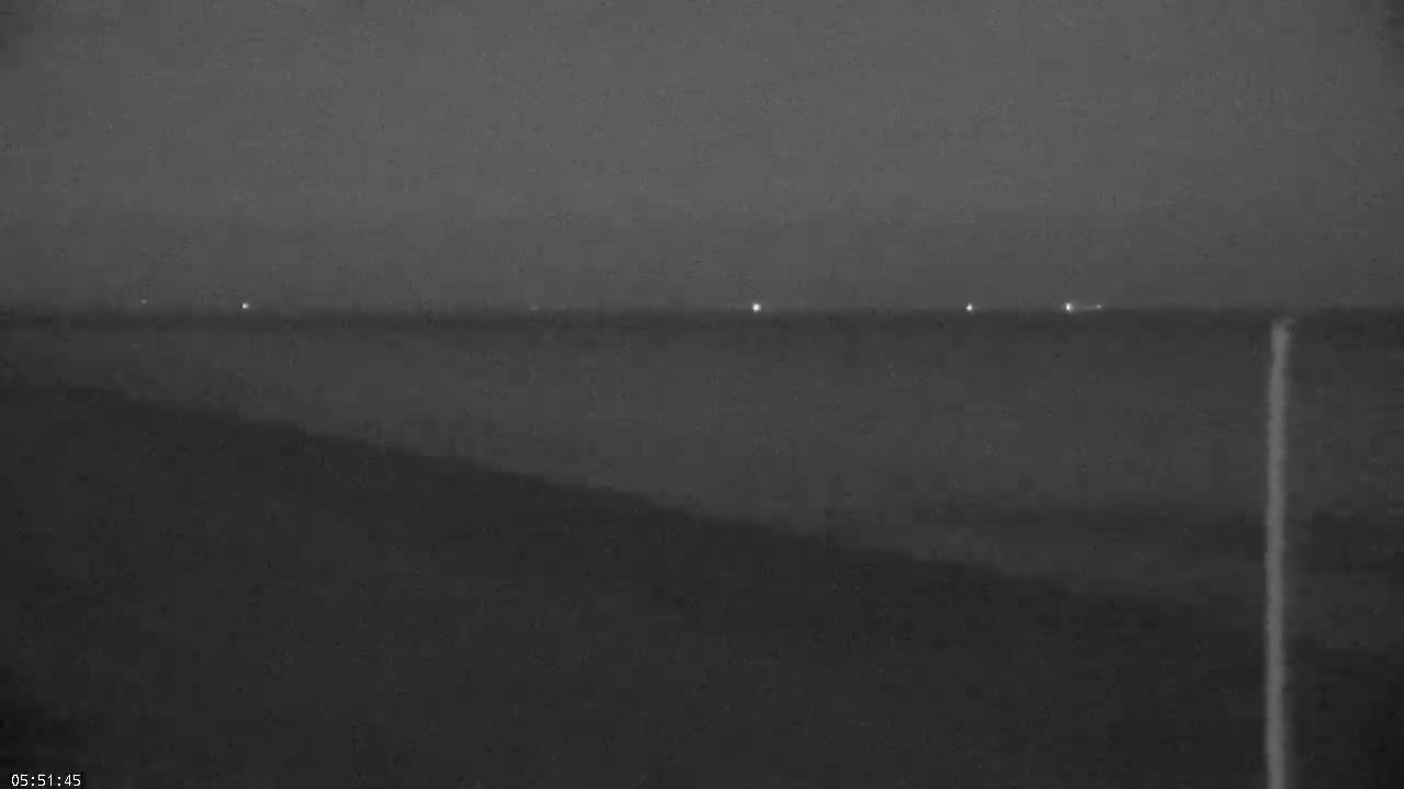 A dark, nighttime landscape shows a body of water with a few distant lights visible on the horizon.
