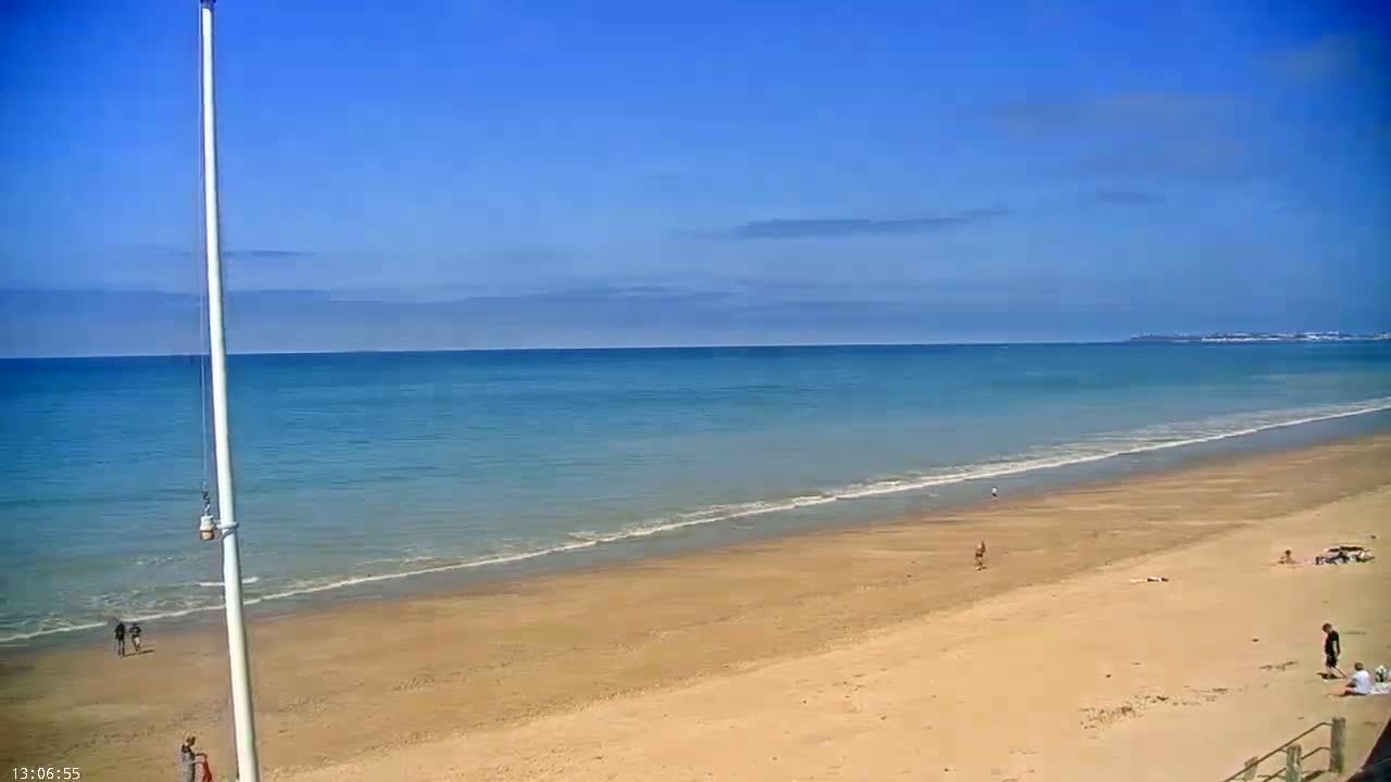 A sandy beach stretches towards a calm, blue ocean under a clear, sunny sky.