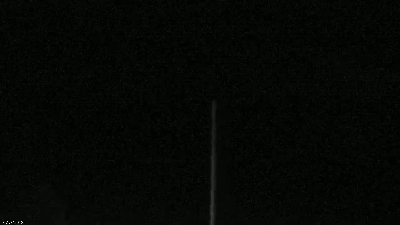 A faint, vertical streak of light is visible against a dark, night sky.