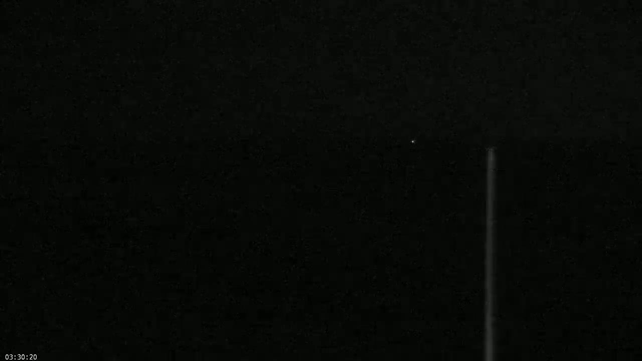 A nighttime image shows a bright vertical light streak against a dark sky with a faint star visible.
