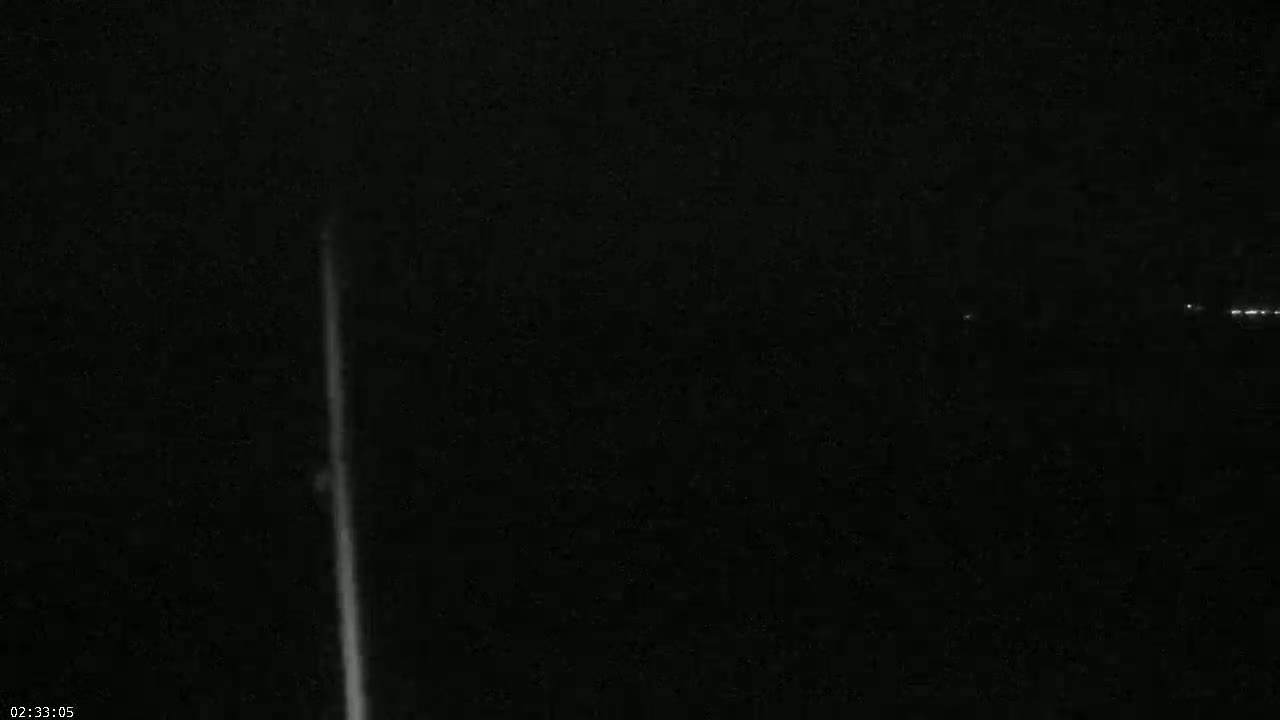 A bright vertical line is visible against a dark, nighttime background with a few distant lights.