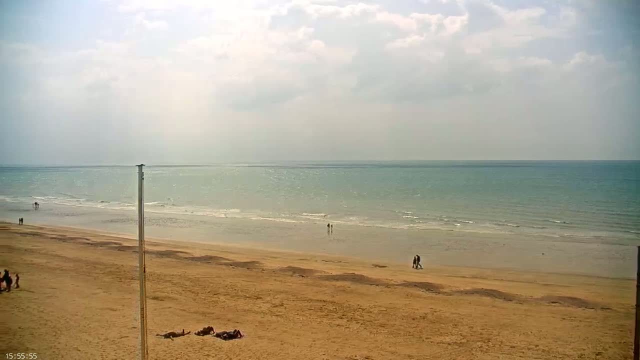 A sandy beach slopes down to a calm, light-blue ocean under a partly cloudy sky.