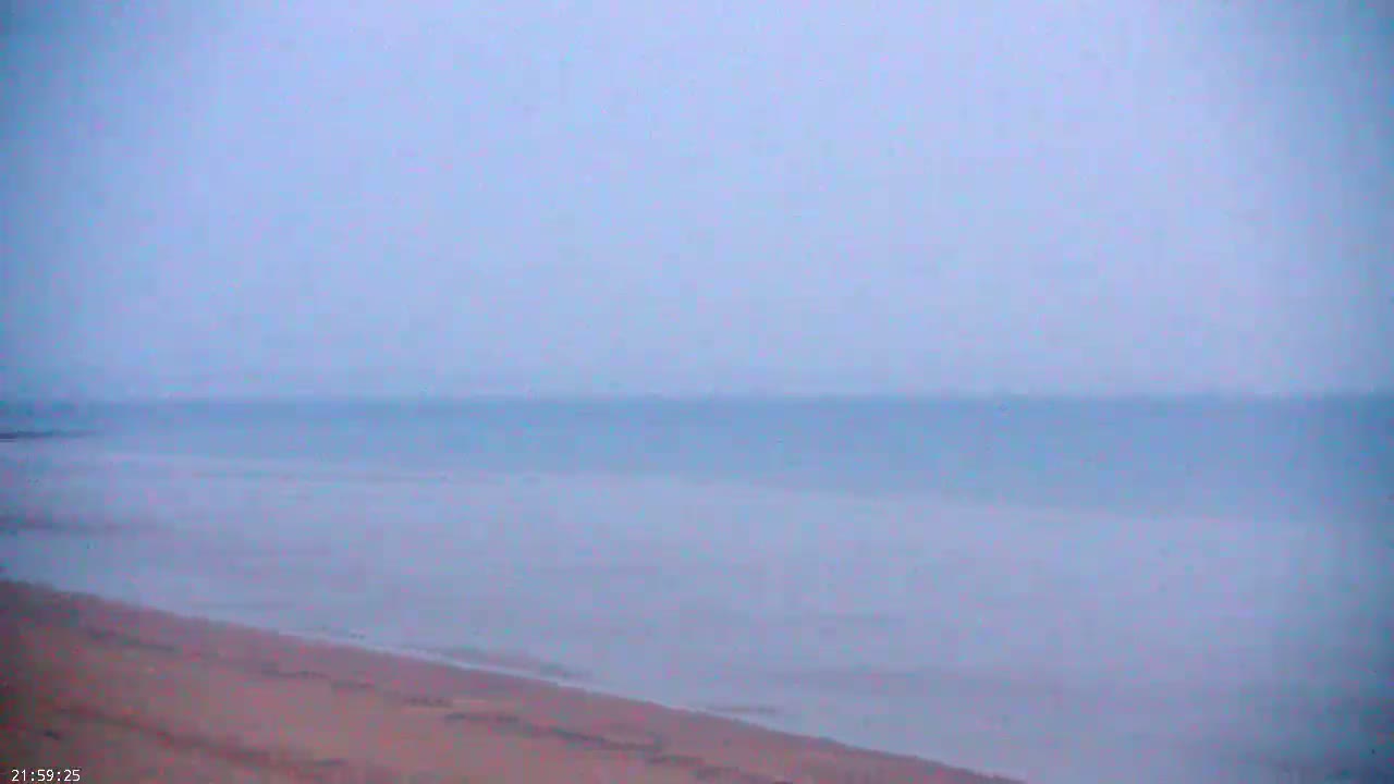 A hazy, overcast sky overlooks a calm body of water meeting a sandy beach.