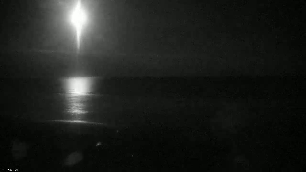 A bright light shines over a dark body of water at night.