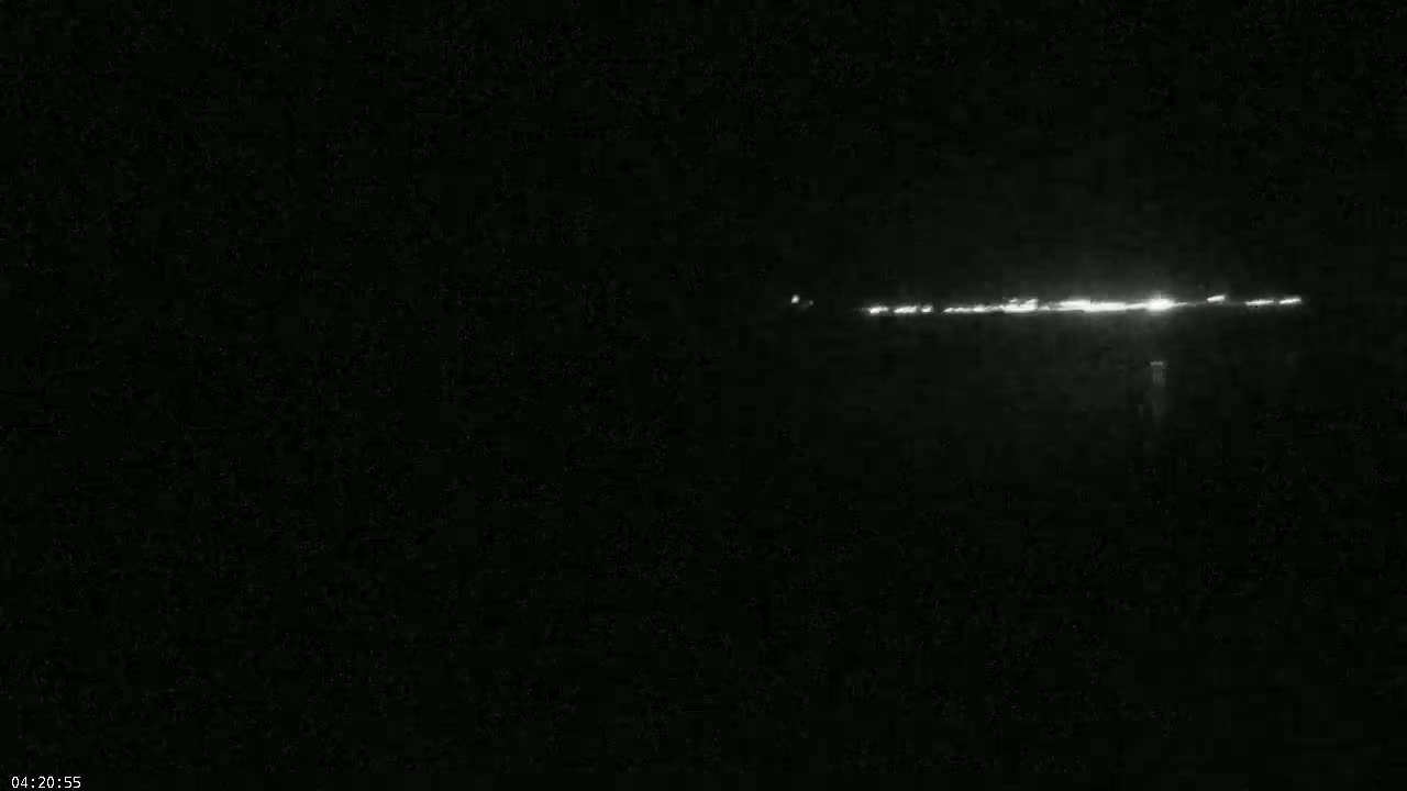 A long, thin line of lights is visible in the distance on a dark, nighttime landscape.