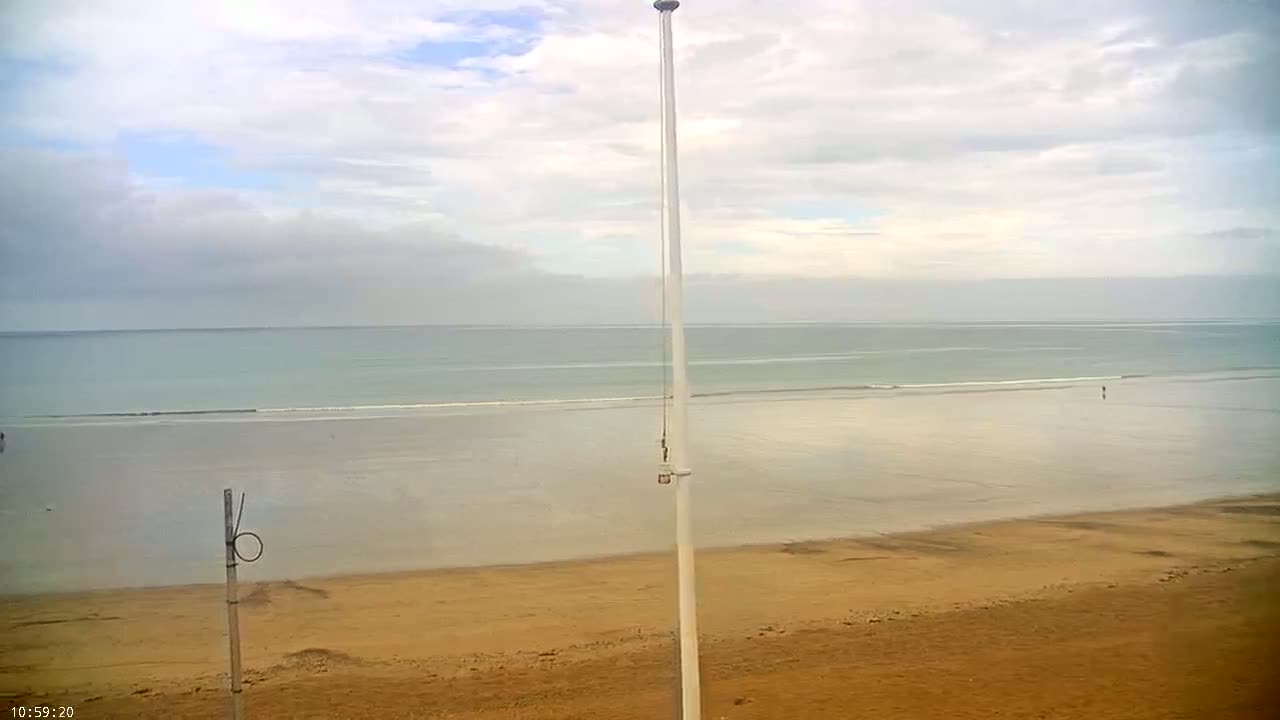 A wide, sandy beach stretches to a calm, light-blue ocean under a mostly cloudy sky.