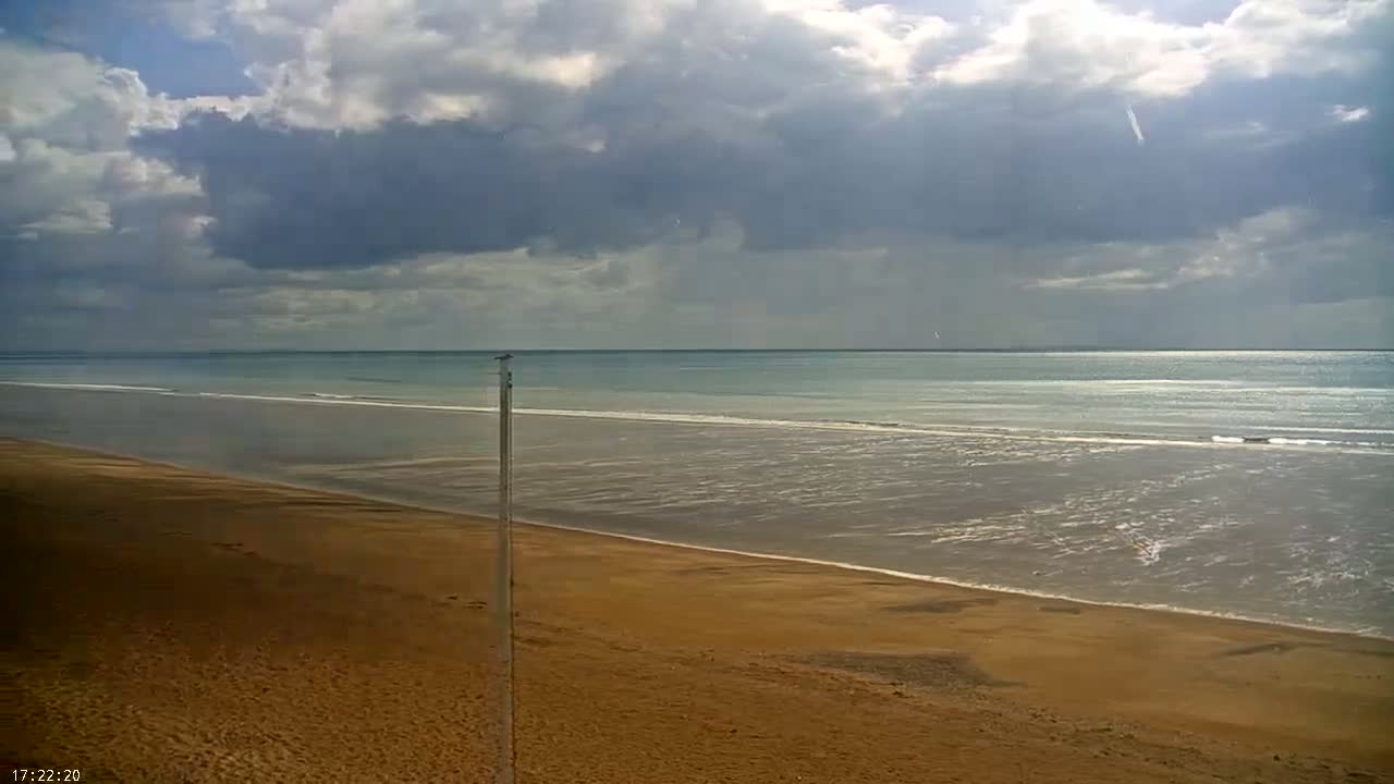 A wide sandy beach stretches toward a calm ocean under a partly cloudy sky.