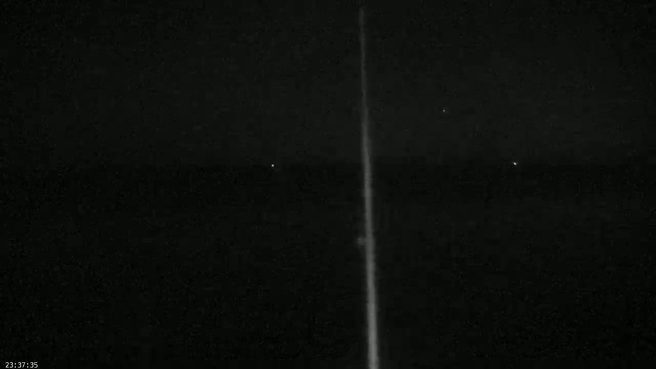 A bright, vertical streak of light is visible against a dark, clear night sky with a few faint distant lights.