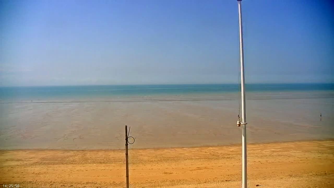 A sandy beach stretches to a calm, light-blue ocean under a clear blue sky.