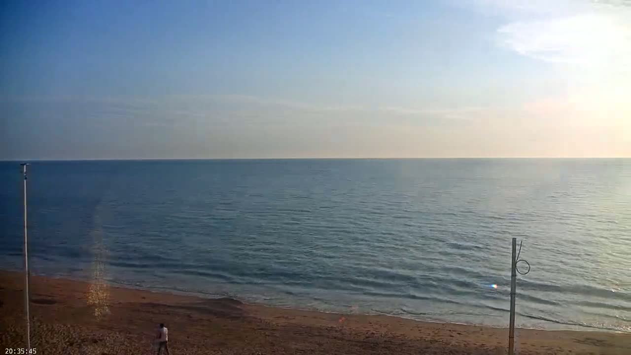 A sandy beach slopes gently down to a calm, blue sea under a clear, light-blue sky.