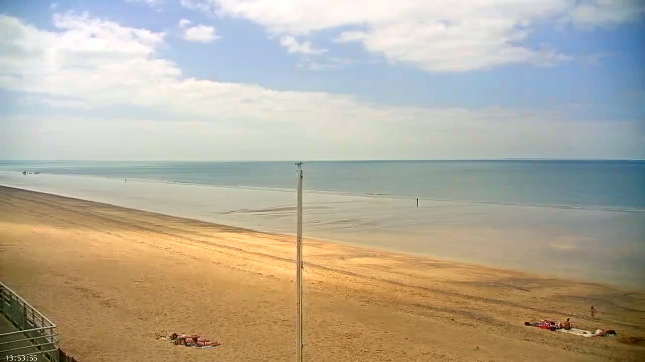 A wide sandy beach stretches to a calm, light-blue ocean under a partly cloudy sky.