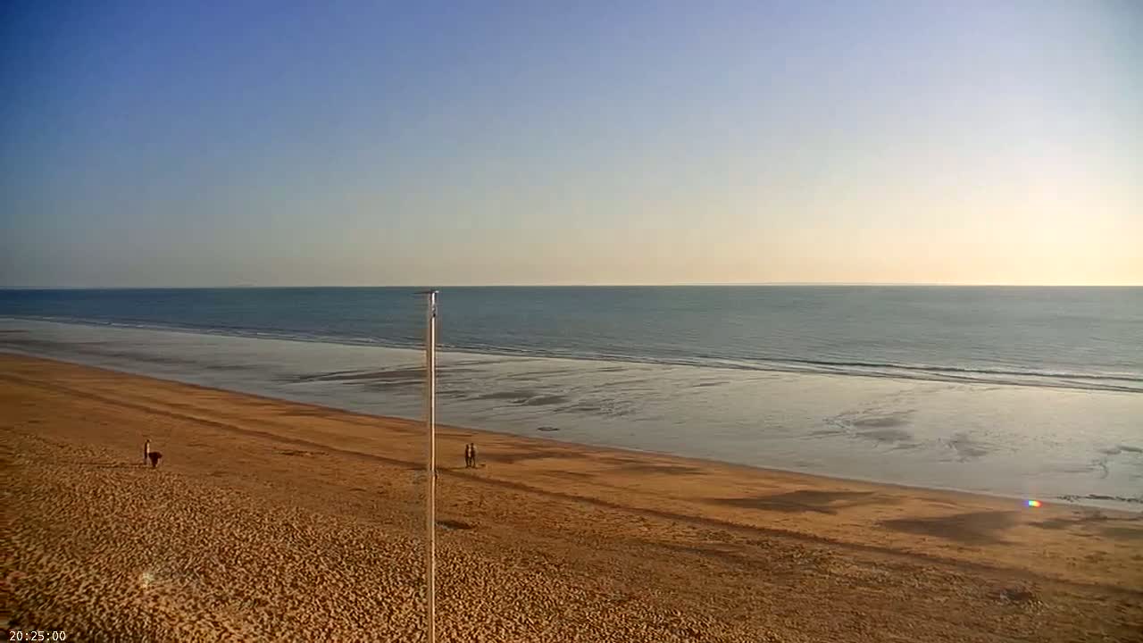 A wide sandy beach stretches to a calm ocean under a clear blue sky.