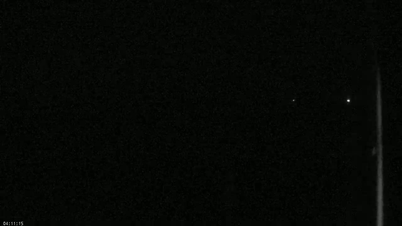 A dark nighttime scene shows two faint lights in the distance and a bright vertical line on the right.
