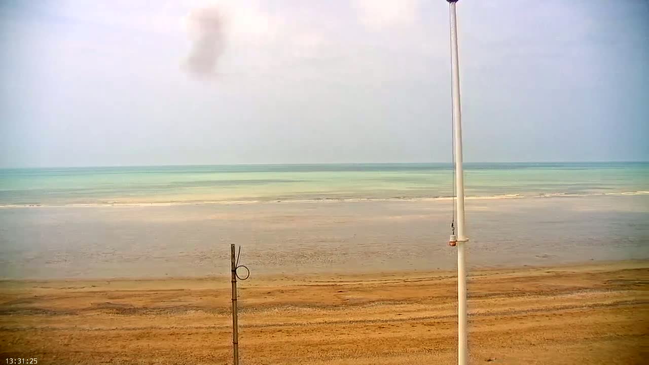 A sandy beach stretches to a calm, light-green ocean under an overcast sky.