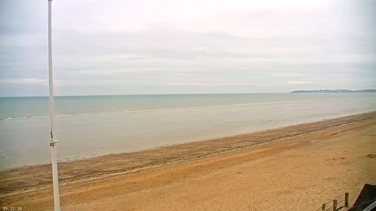 A wide sandy beach stretches to a calm, light-grey ocean under an overcast sky.