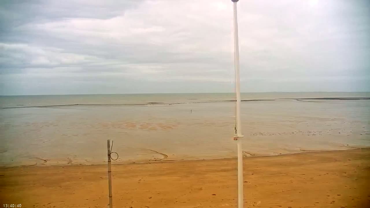 A tan beach stretches to a calm, grey-toned ocean under a cloudy sky.
