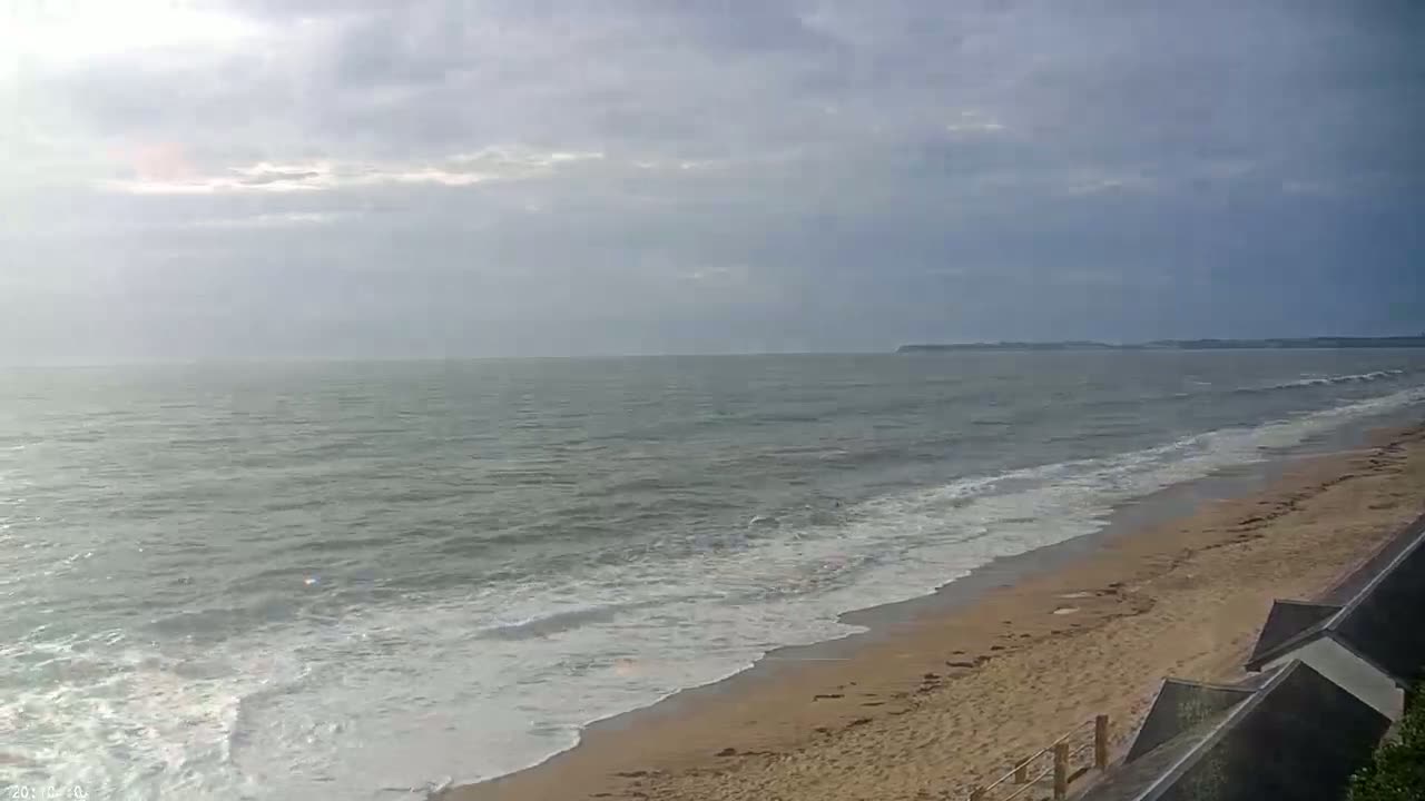 A sandy beach with gentle waves rolling onto the shore under a mostly cloudy sky.