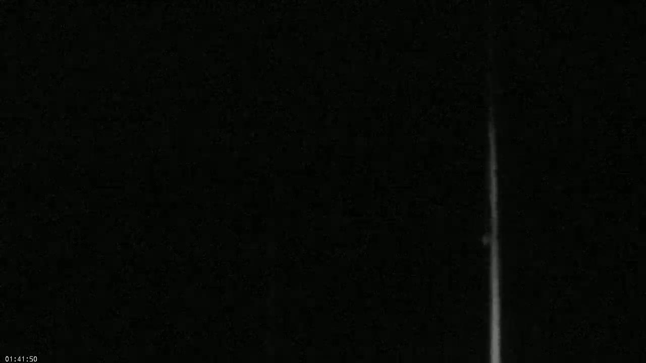 A bright, vertical streak of light is visible against a completely dark night sky.