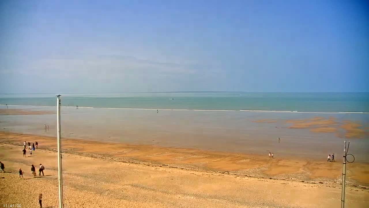 A wide sandy beach stretches out to a calm, light teal ocean under a clear blue sky.