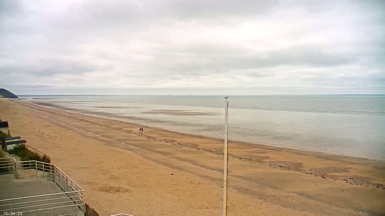 A long, sandy beach stretches out to a calm, gray sea under an overcast sky.